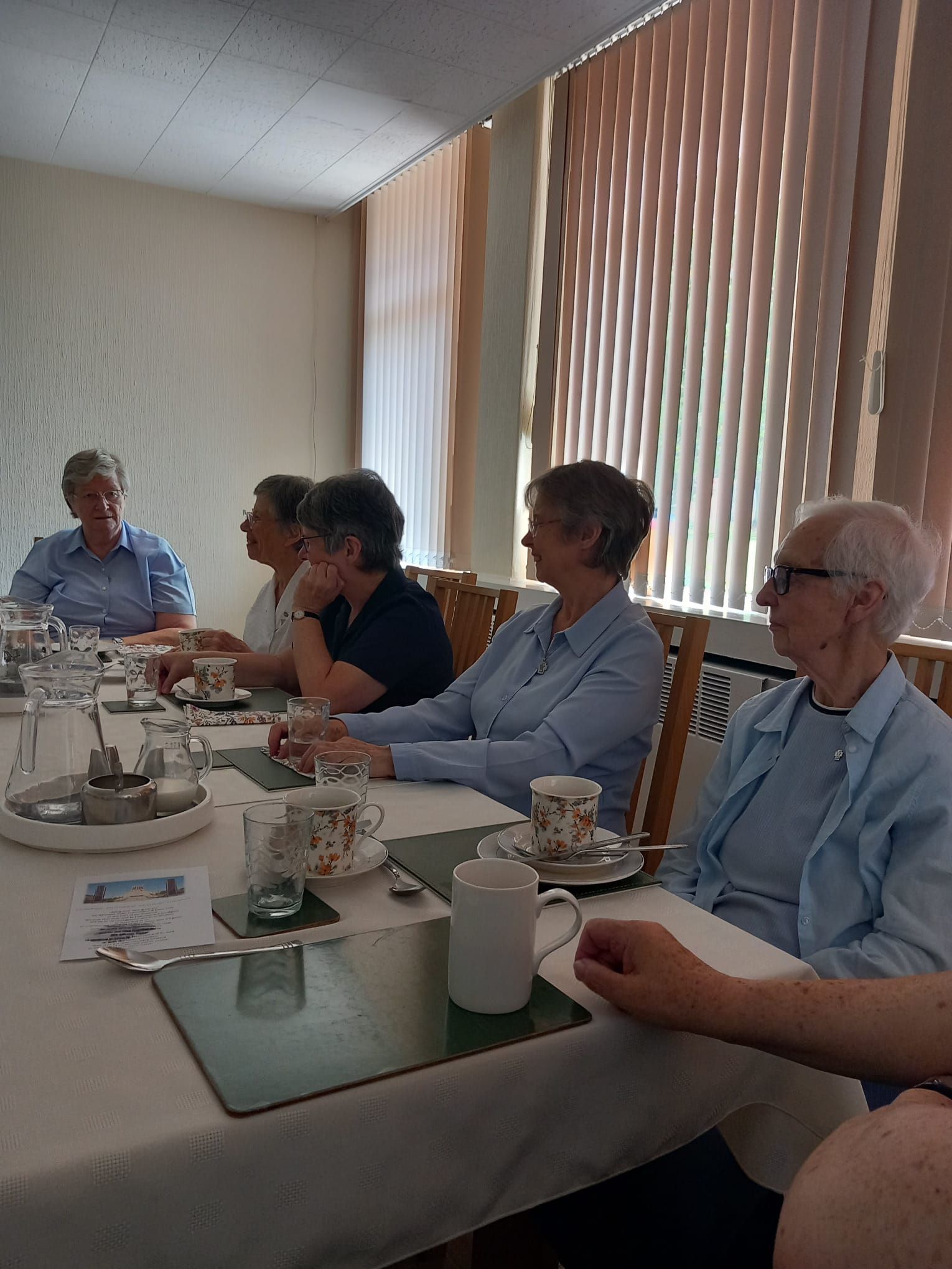 A group of people are sitting at a table with cups and saucers.