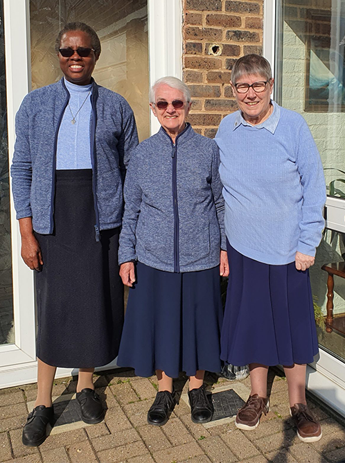 three daughters of charity are standing next to each other in front of a brick building .