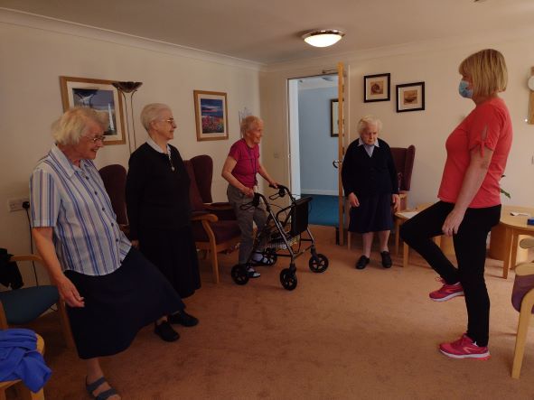 A group of elderly women are doing exercises in a living room