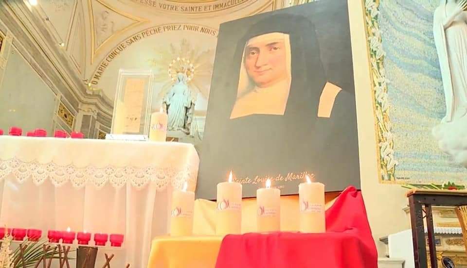 A painting of a woman is on a table with candles in a church.