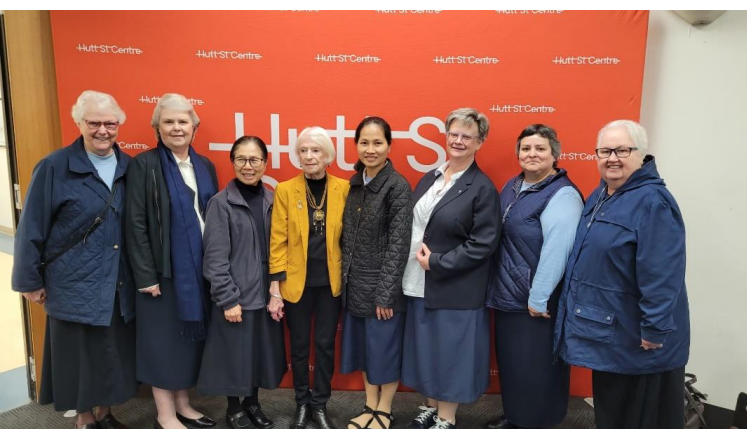 A group of women are posing for a picture in front of a red wall.