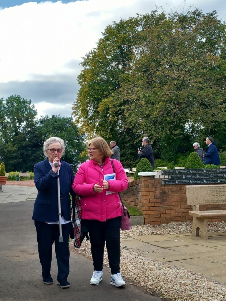 Two older women are walking down a sidewalk in a park.