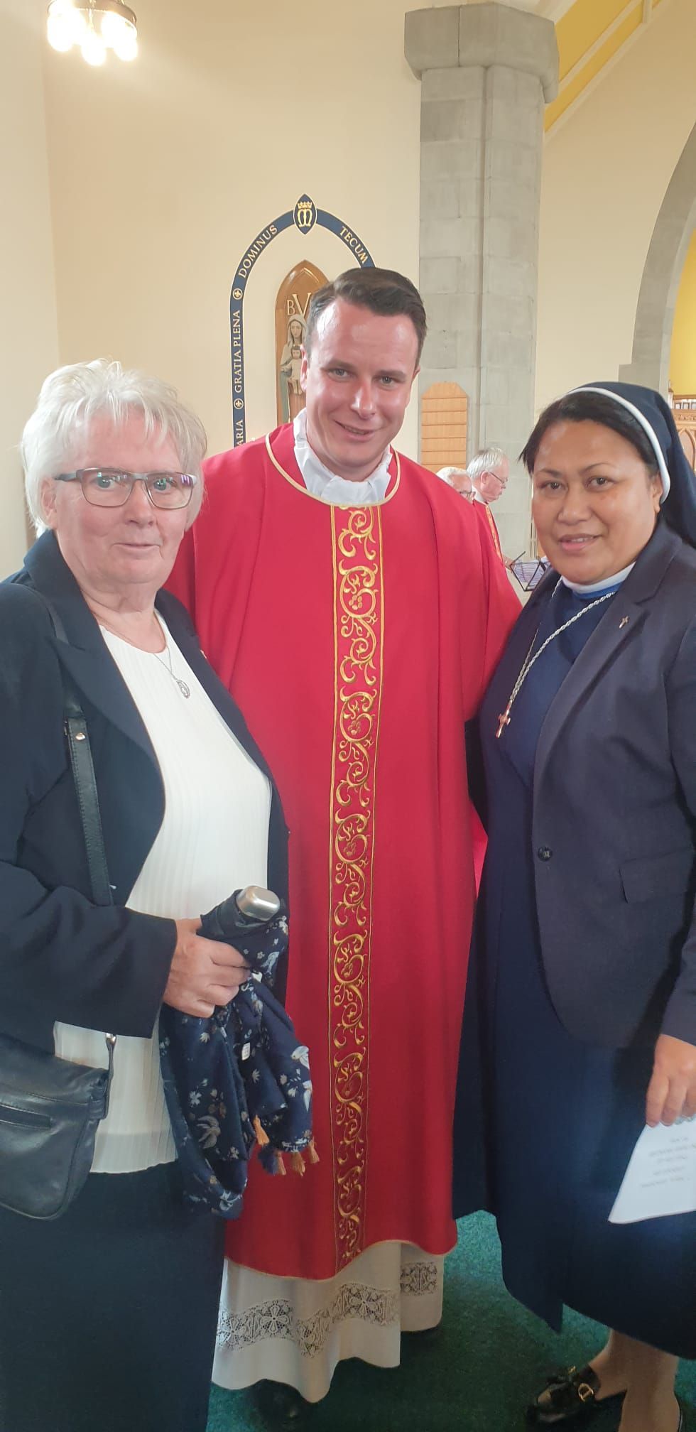 A man in a red robe is standing next to two women in a church.