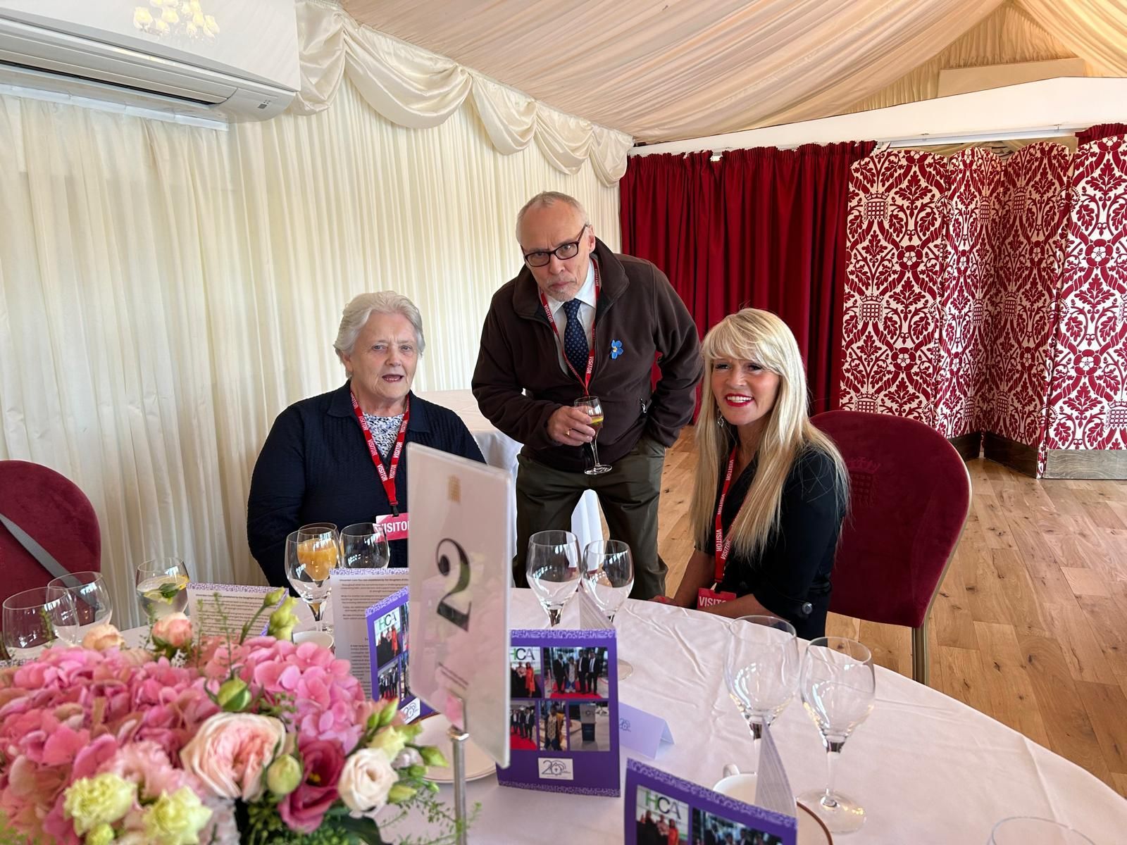 A group of people are sitting at a table with flowers and wine glasses.