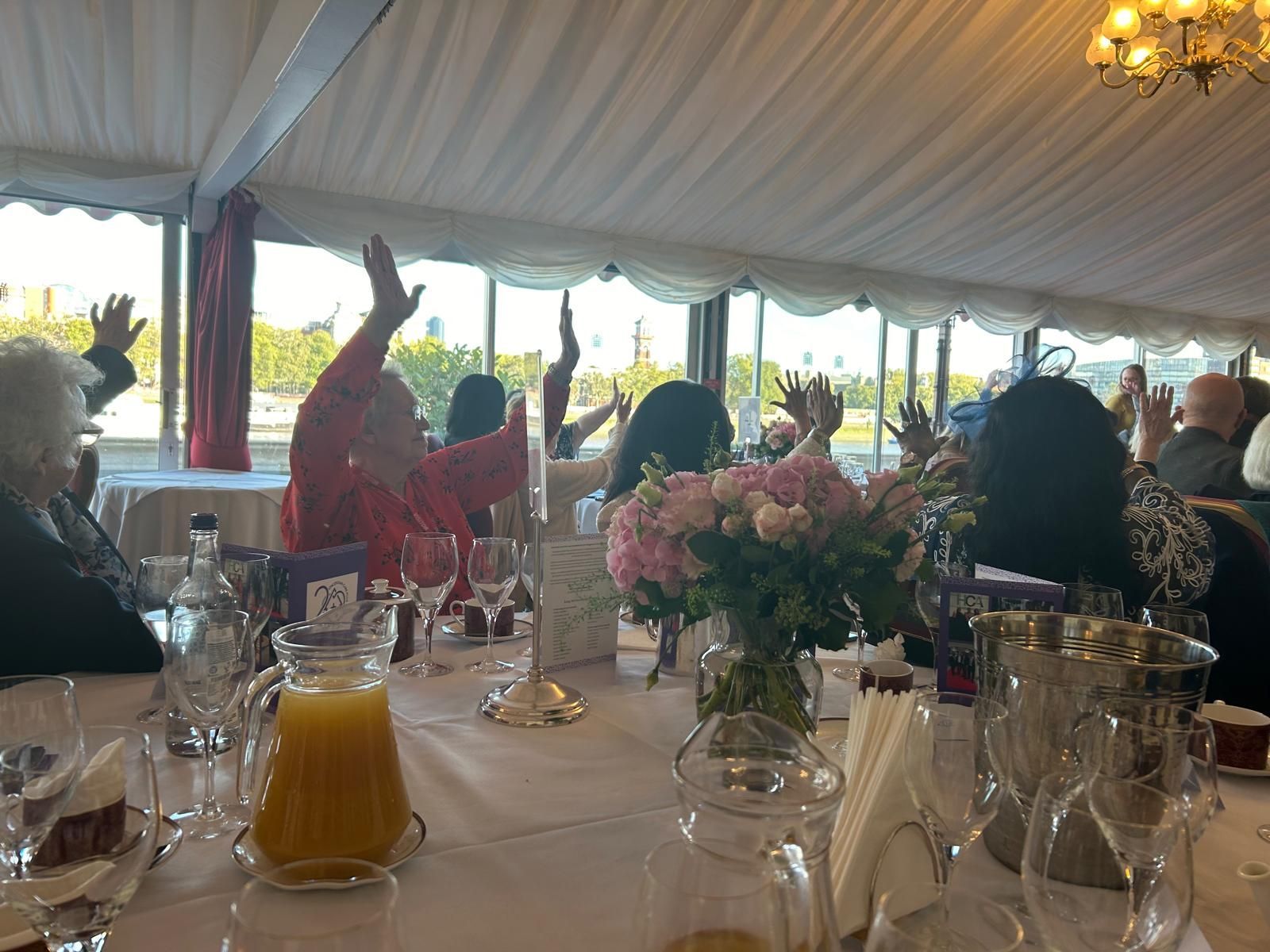 A group of people are sitting at a table with their hands in the air.