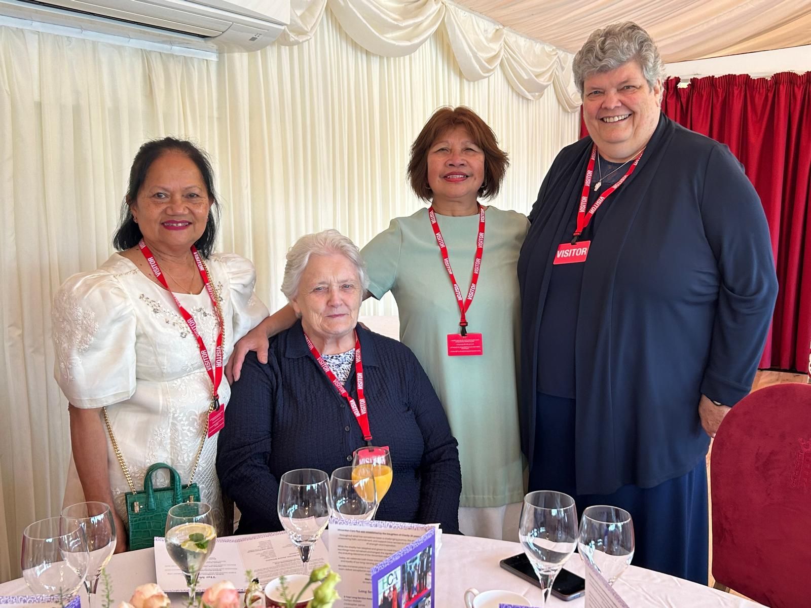 A group of women are posing for a picture while sitting at a table with wine glasses.