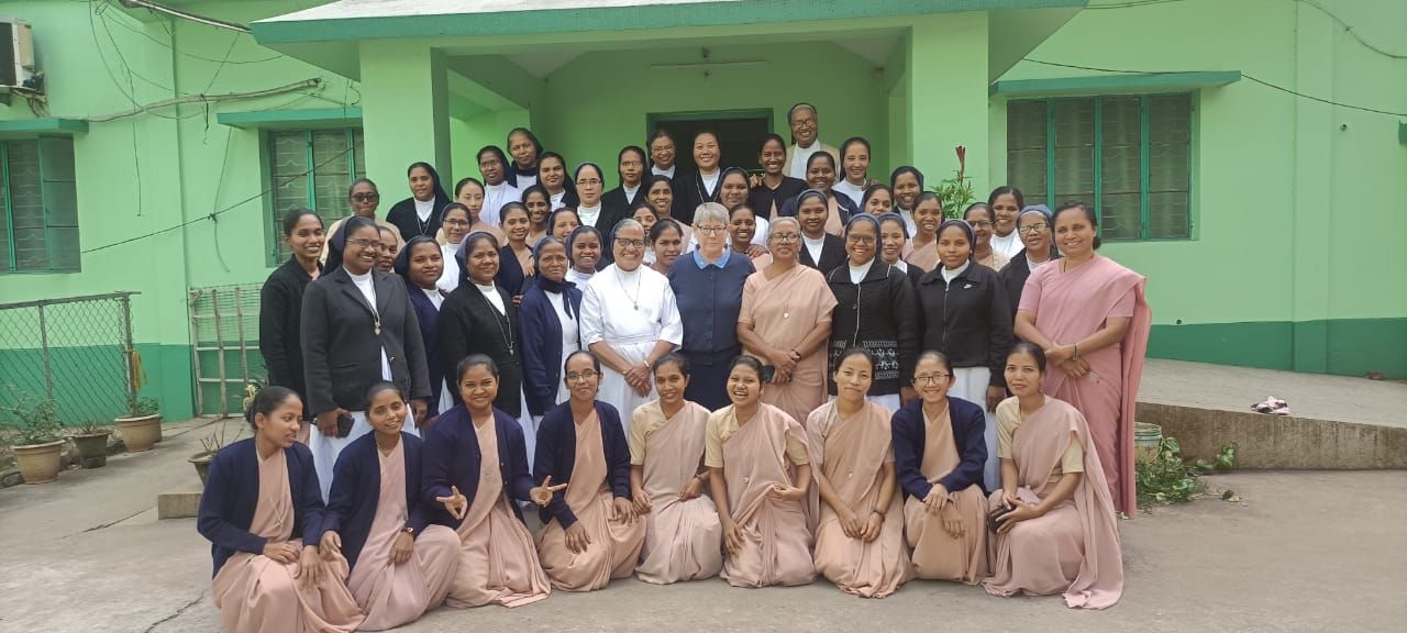 Group photo of women in front of a green building. Some are kneeling. Several are wearing religious attire.