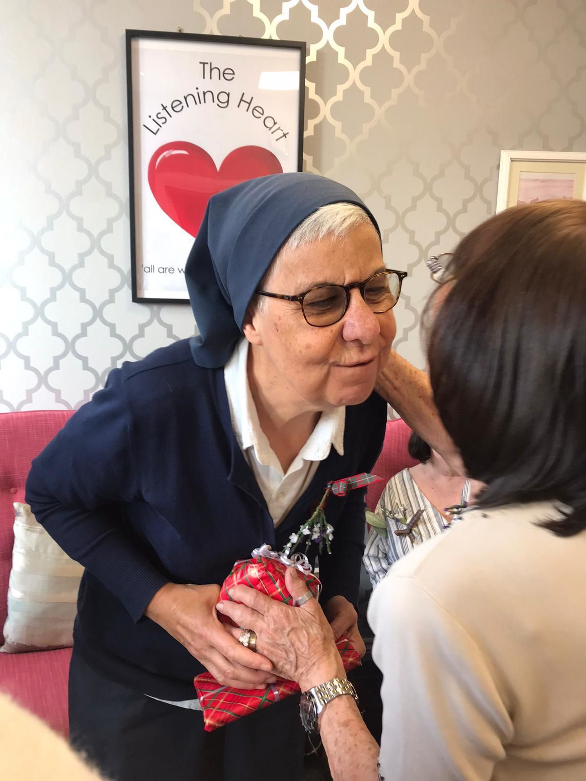 A woman is giving a gift to another woman in front of a poster that says the listening heart