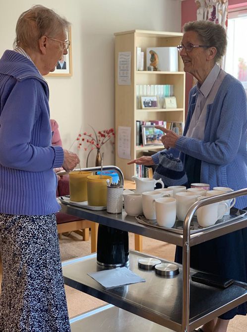 two older sisters are standing next to a cart of coffee cups.