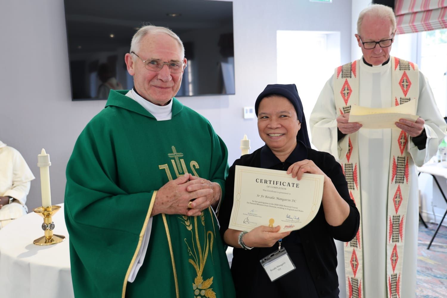 Two priests are standing next to a woman holding a certificate.