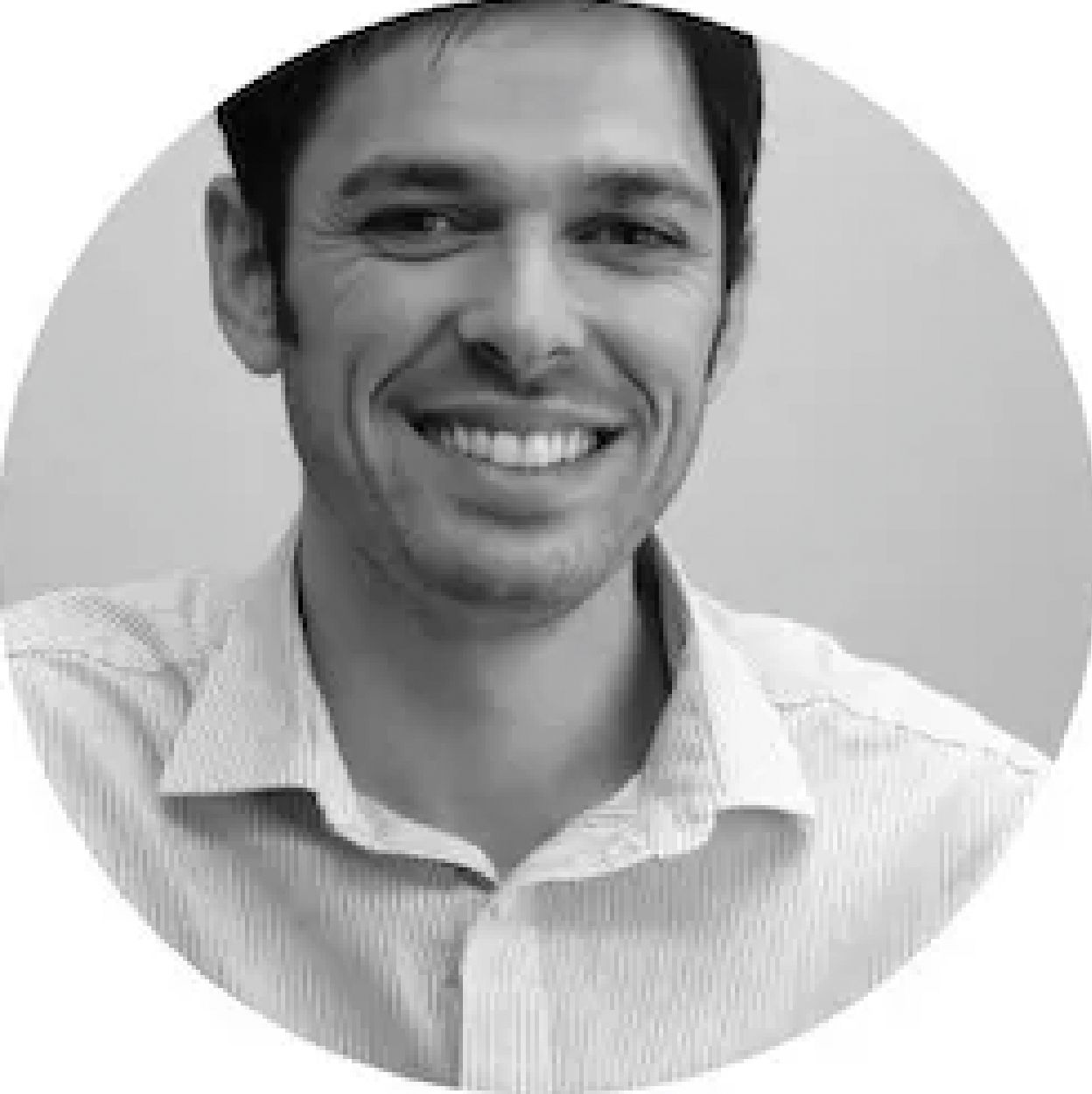 A man in a striped shirt is smiling in a black and white photo.