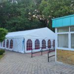 A large white tent with red windows is sitting next to a building.