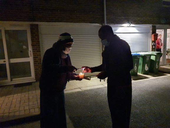 Two people are standing next to each other in the dark holding candles.