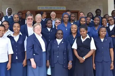 Group of women, mostly in blue uniforms, outside a building; smiling at the camera.
