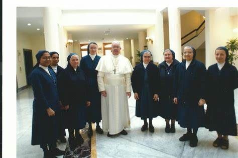 Pope Francis with a group of nuns in a bright hallway. They are smiling.