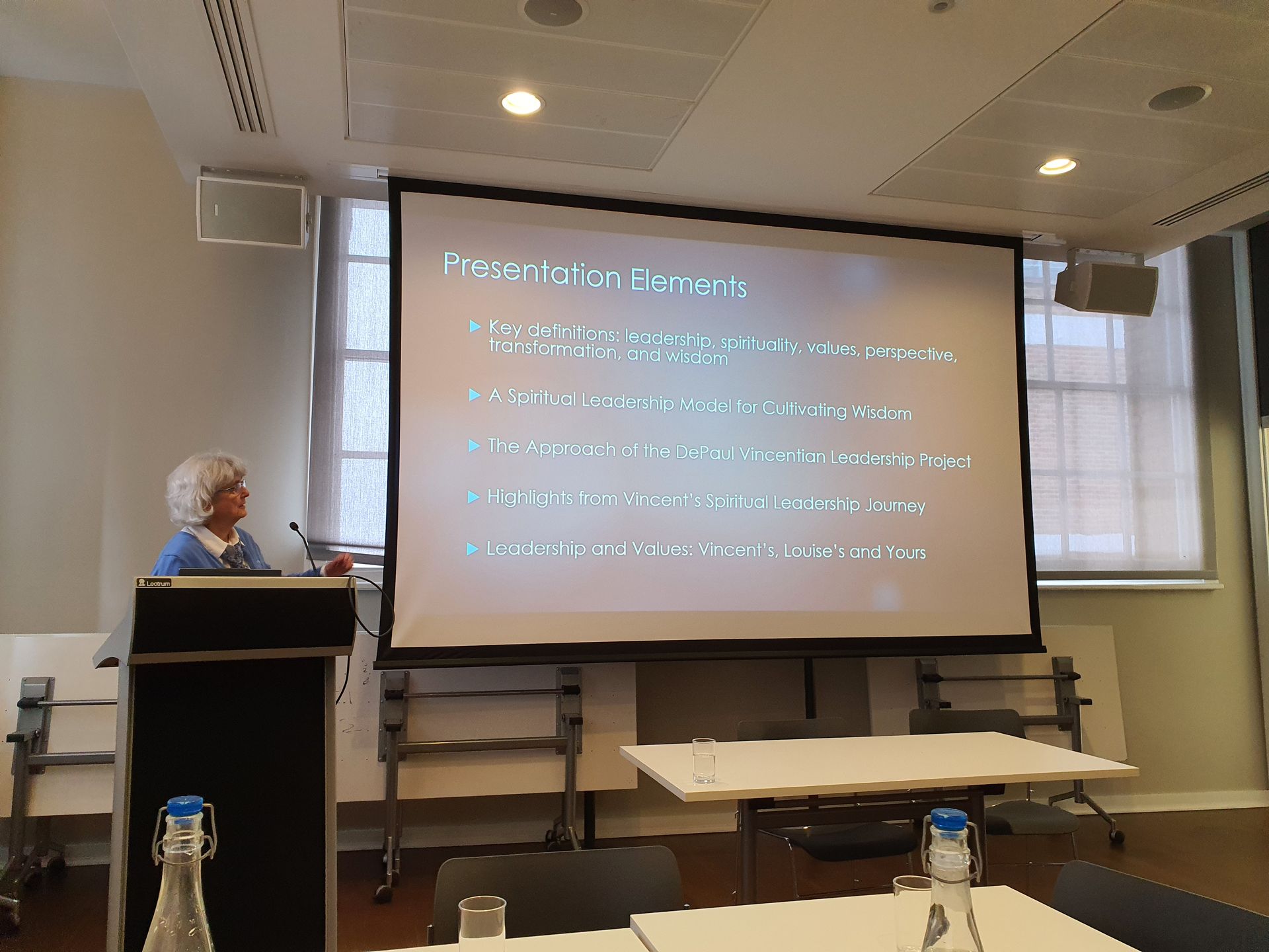 A woman is giving a presentation in front of a large screen