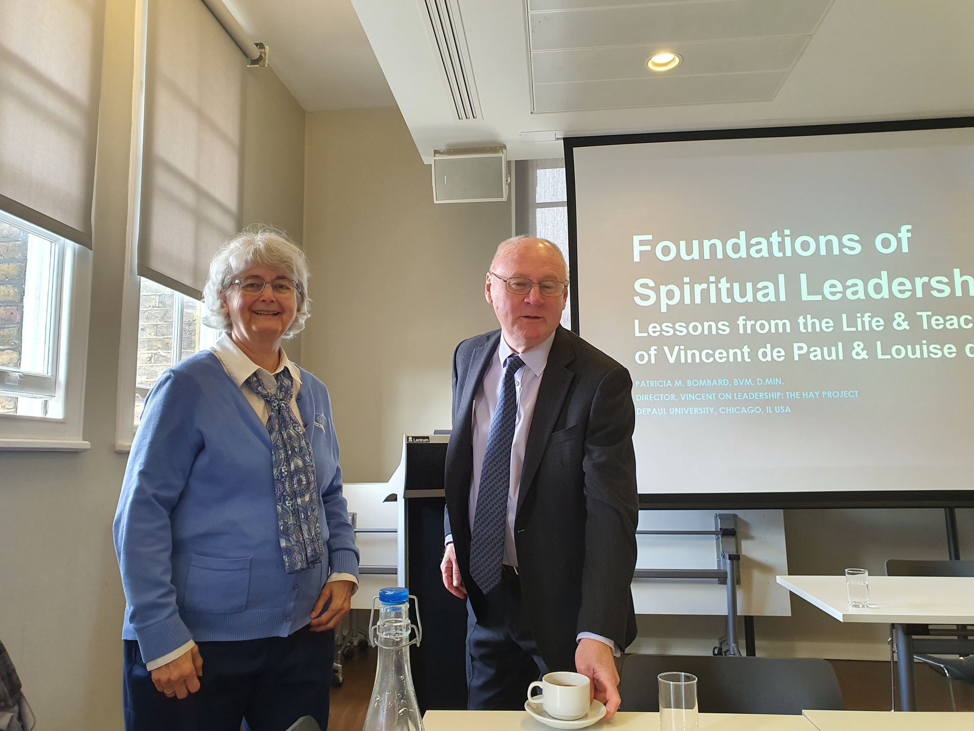 A man and a woman are standing in front of a projector screen that says foundations of spiritual leadership