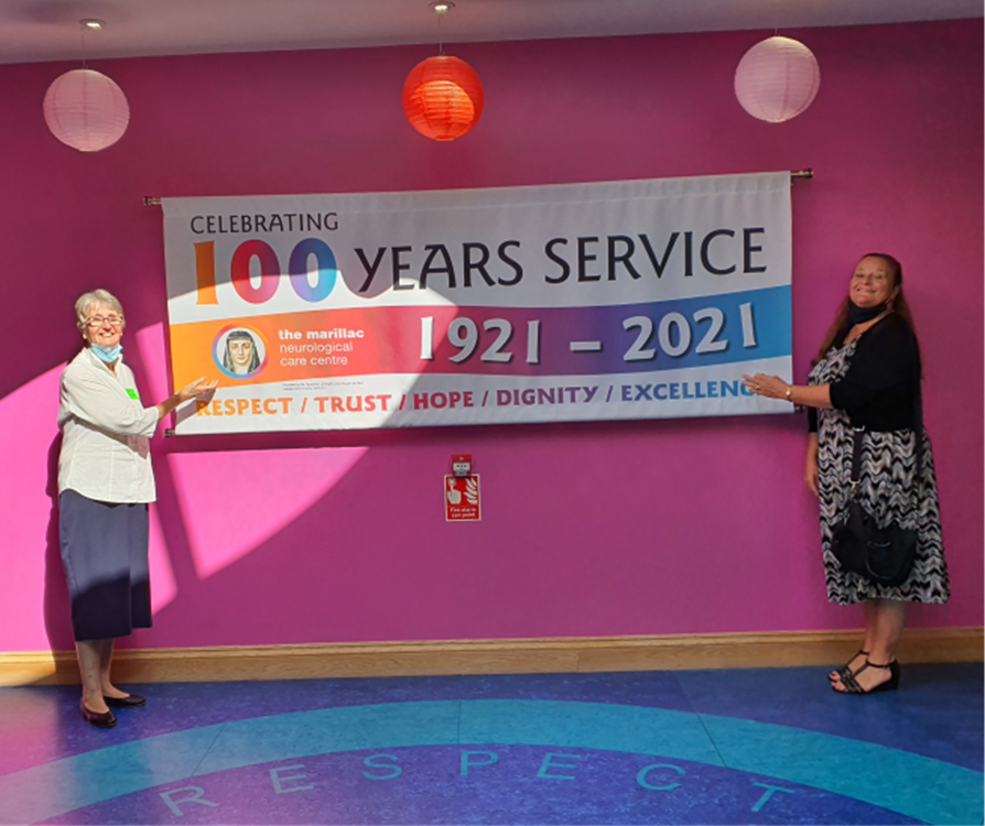 Two women holding a banner that says celebrating 100 years service 1921-2021