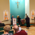 A group of people are sitting in a church with a cross on the wall.