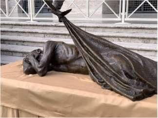 A statue of a man laying on a table with a blanket around him.