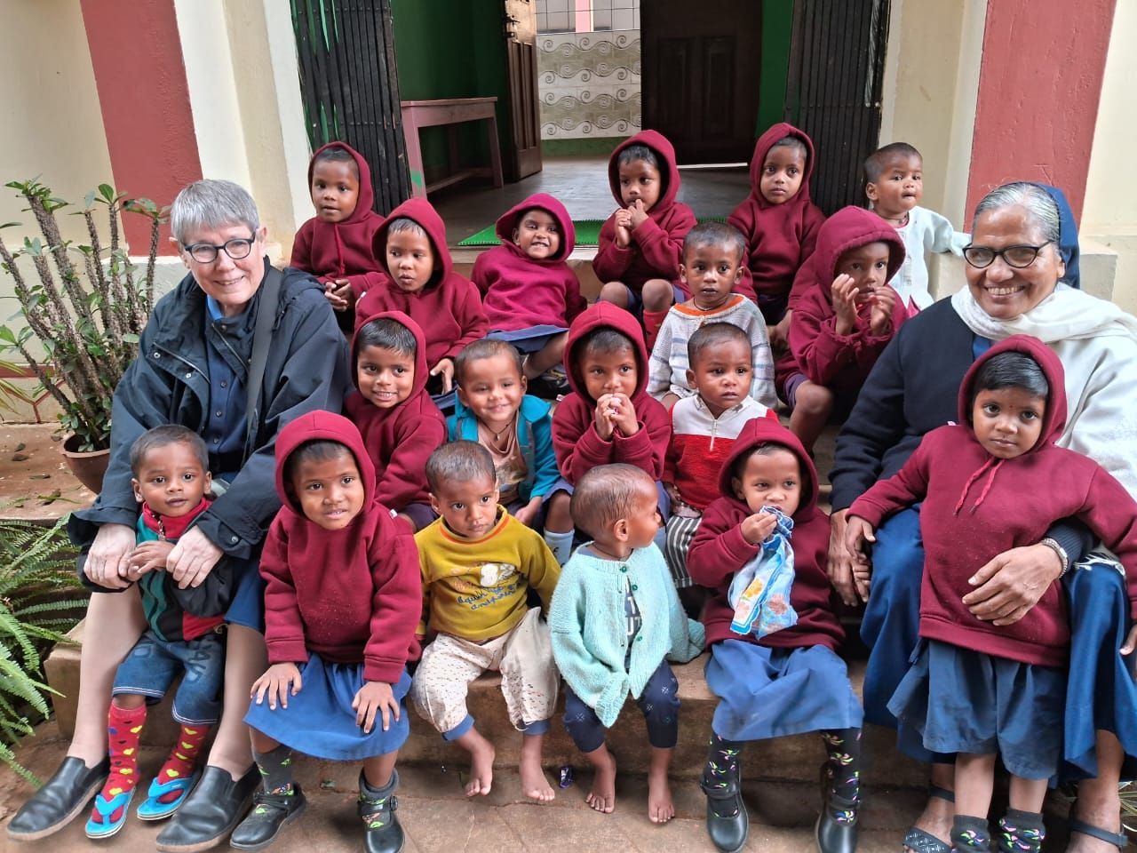 Group photo: Two women with children in maroon hoodies, posing outdoors.