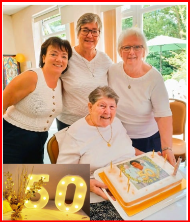 Four women, one holding a cake with a photo, celebrating a 50th birthday.