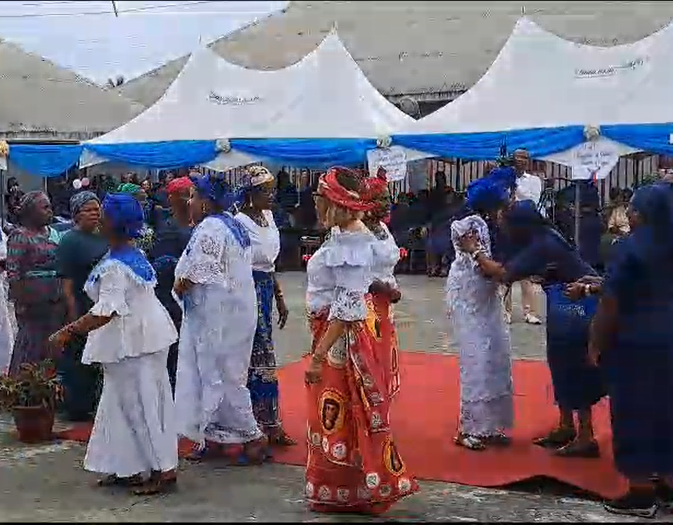 A group of women are dancing on a red carpet in front of tents.