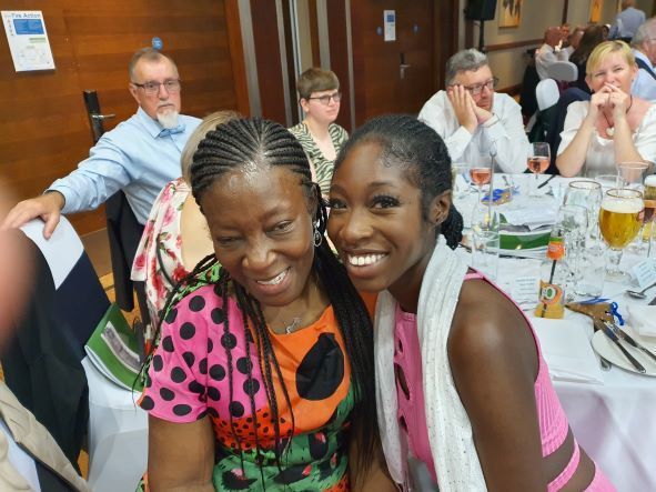 Two women are posing for a picture while sitting at a table.