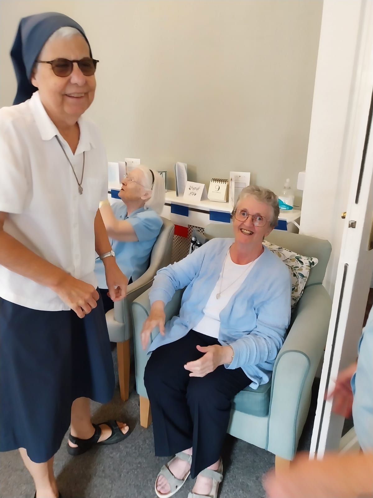 A woman wearing sunglasses is standing next to a woman sitting in a chair