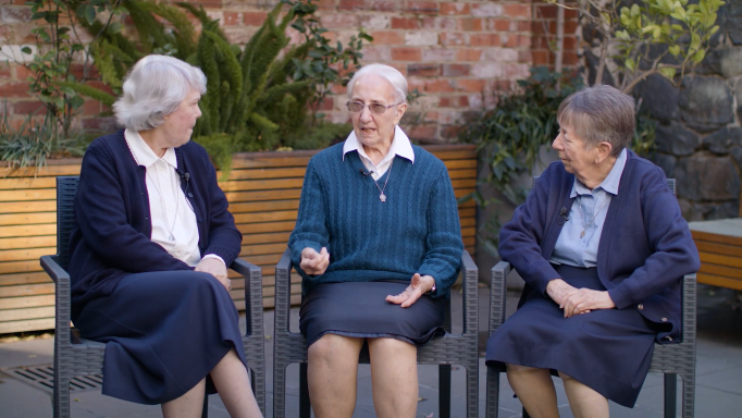 Three older women are sitting in chairs talking to each other.