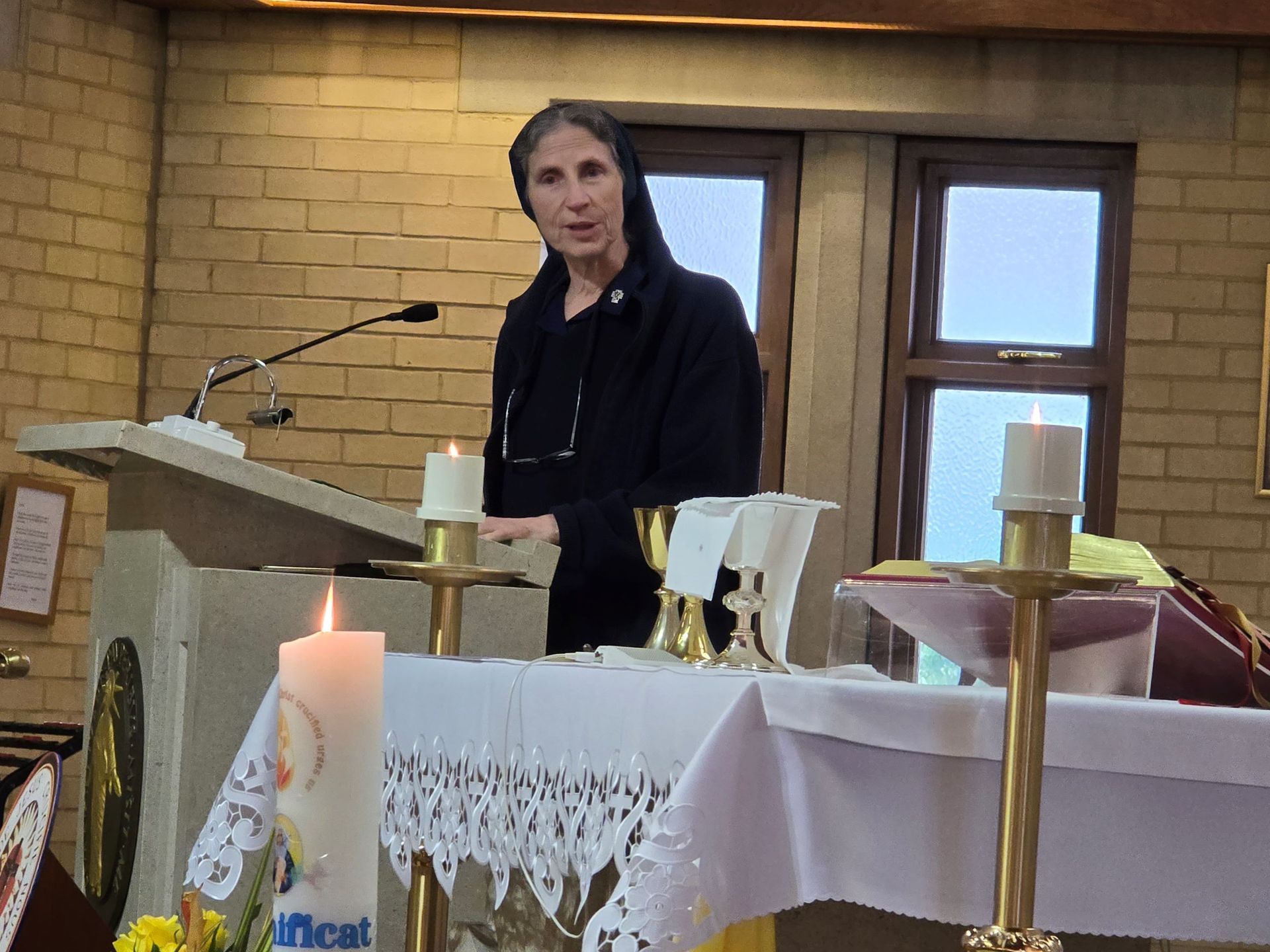 A woman is standing in front of an altar with candles and a microphone.