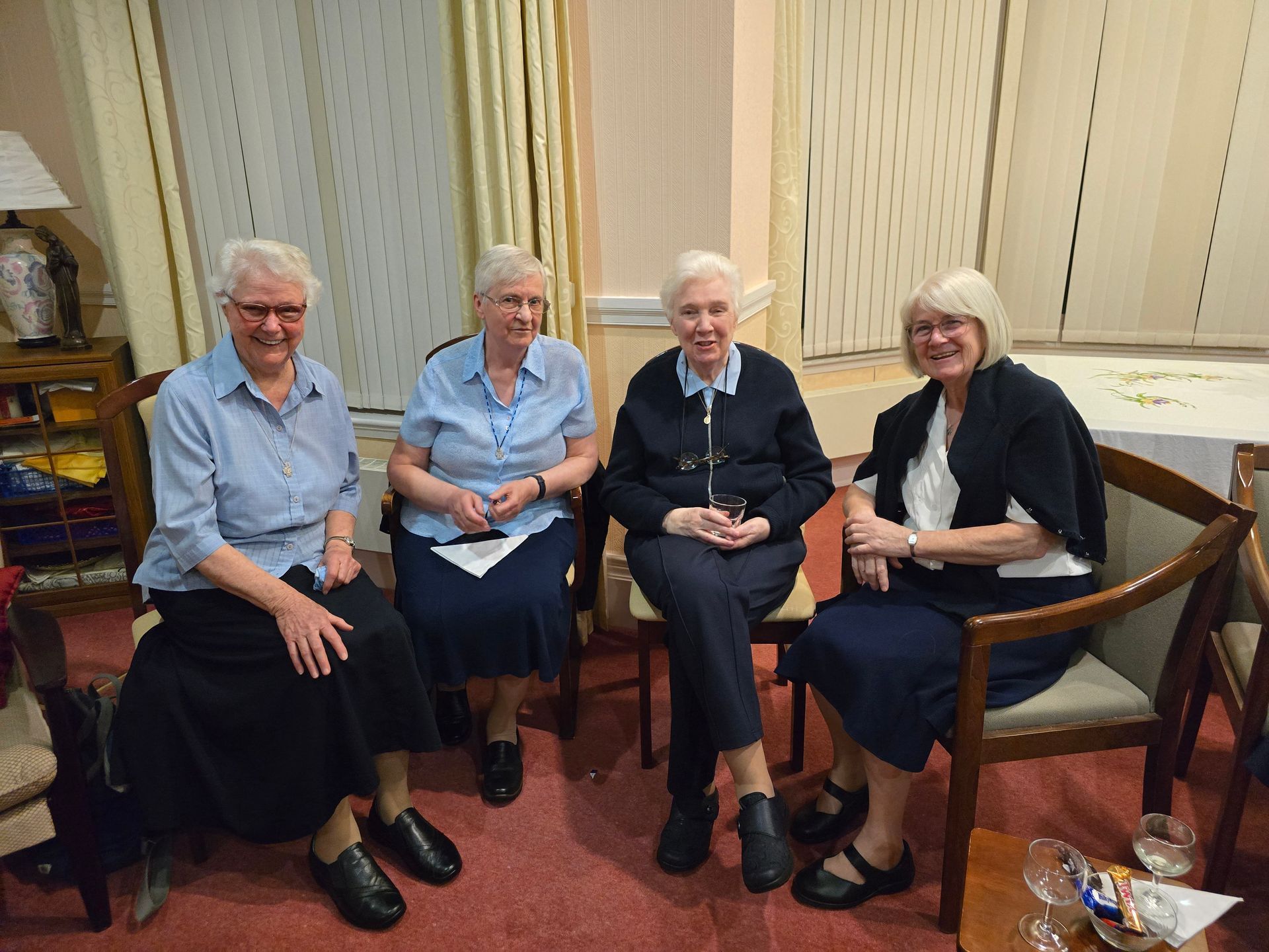 Four older women are sitting in chairs in a living room.