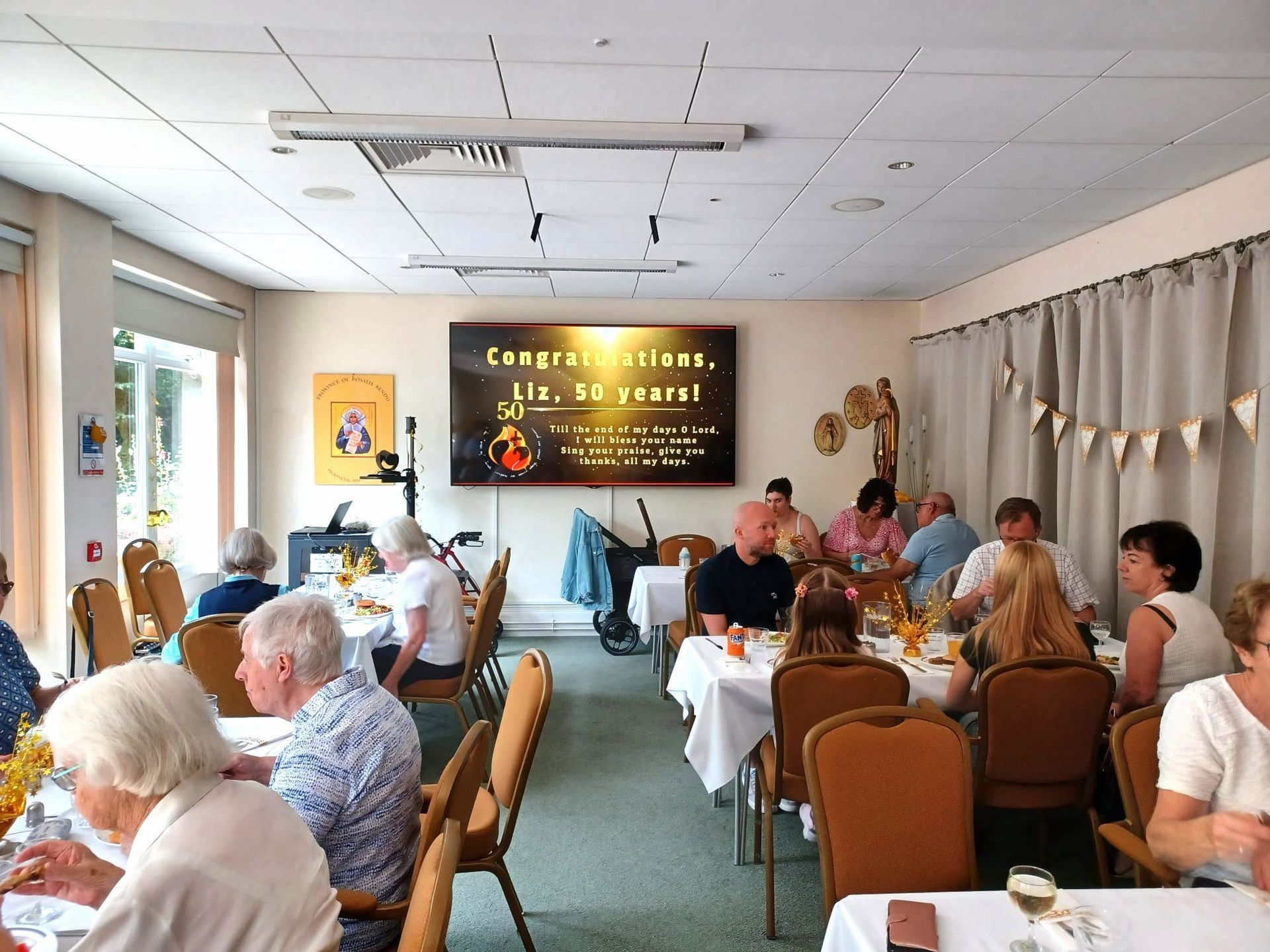 People at a party with tables set for a meal; a screen says 