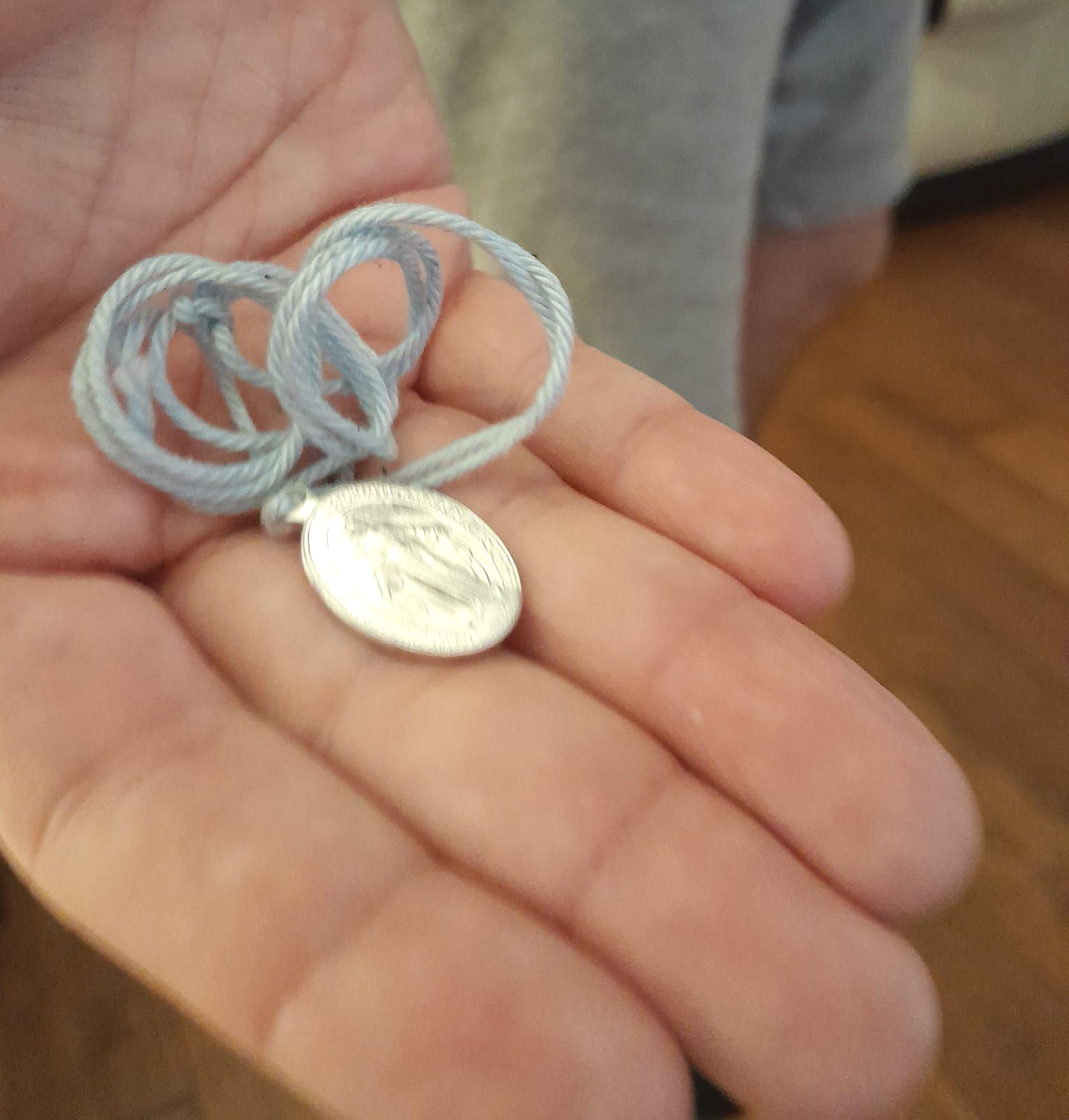 Hand holding a light blue cord necklace with a silver medallion.