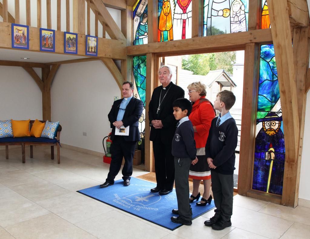 Clergy and children at doorway; stained glass, wooden beams, blue welcome mat.