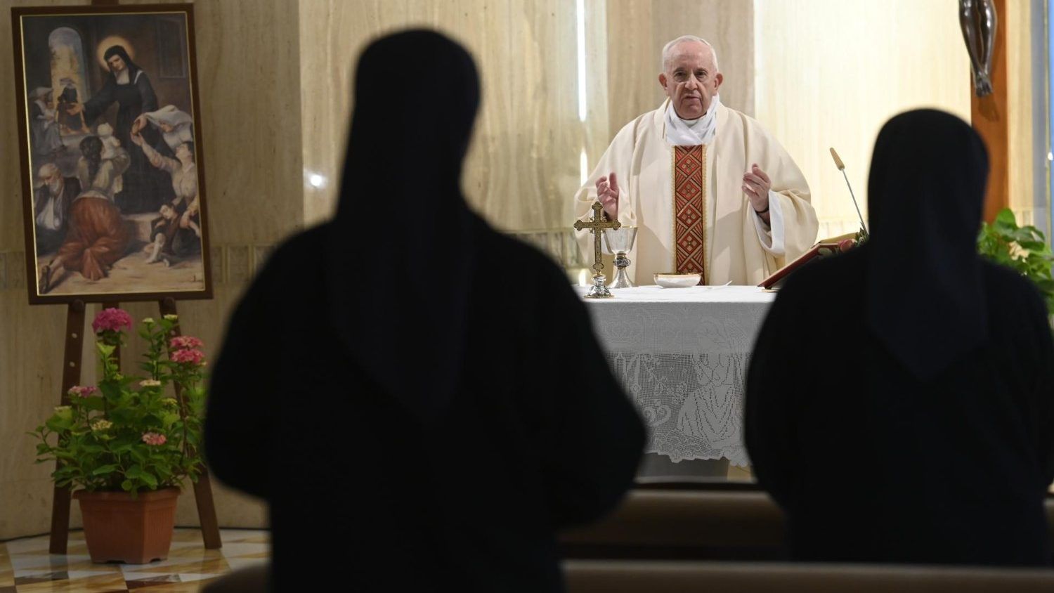 Pope Francis giving mass, facing away from two nuns in dark habits.