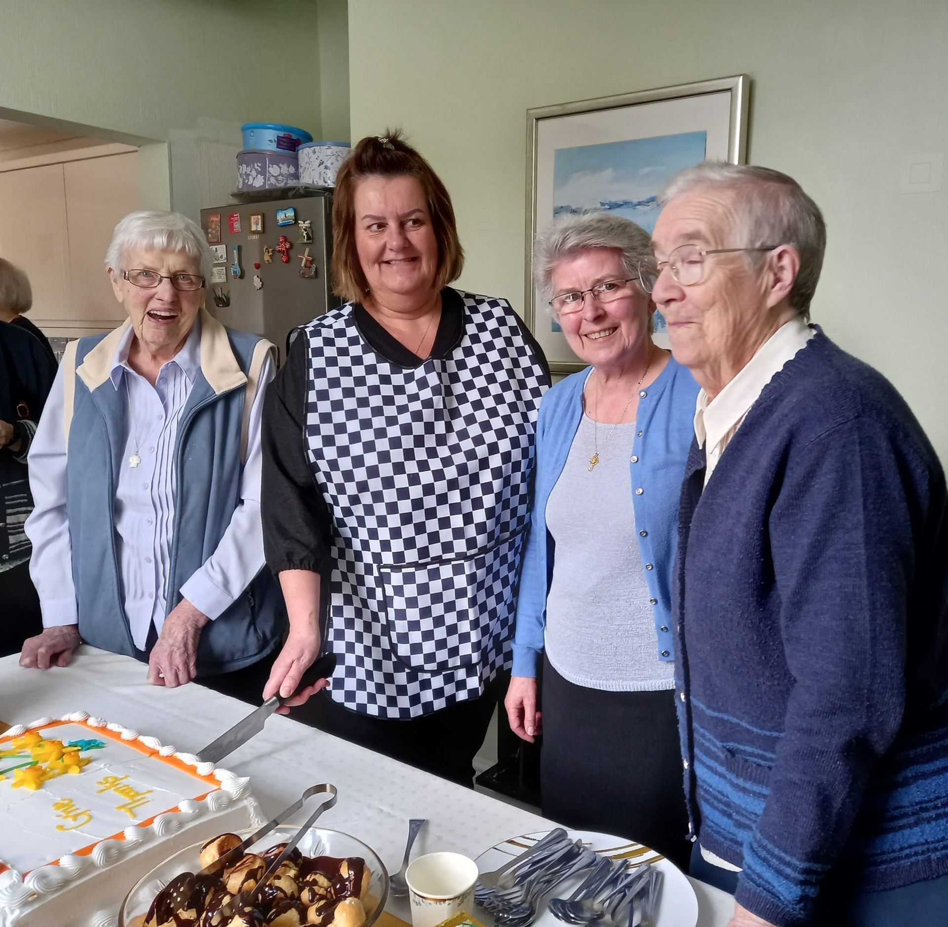 Four people smiling around a cake, likely a birthday celebration. Kitchen setting, cheerful expressions, ready to eat.