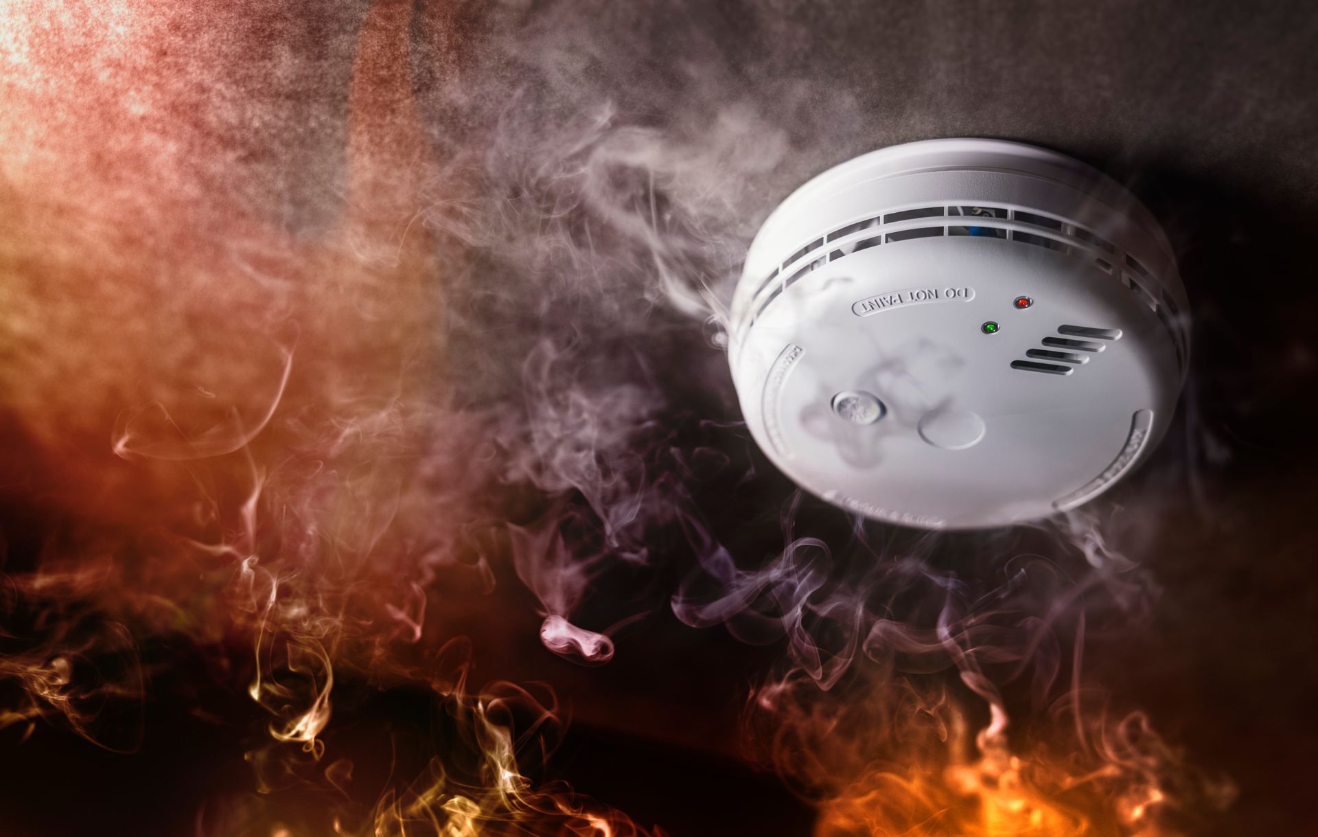 Ceiling smoke detector surrounded by smoke and flames