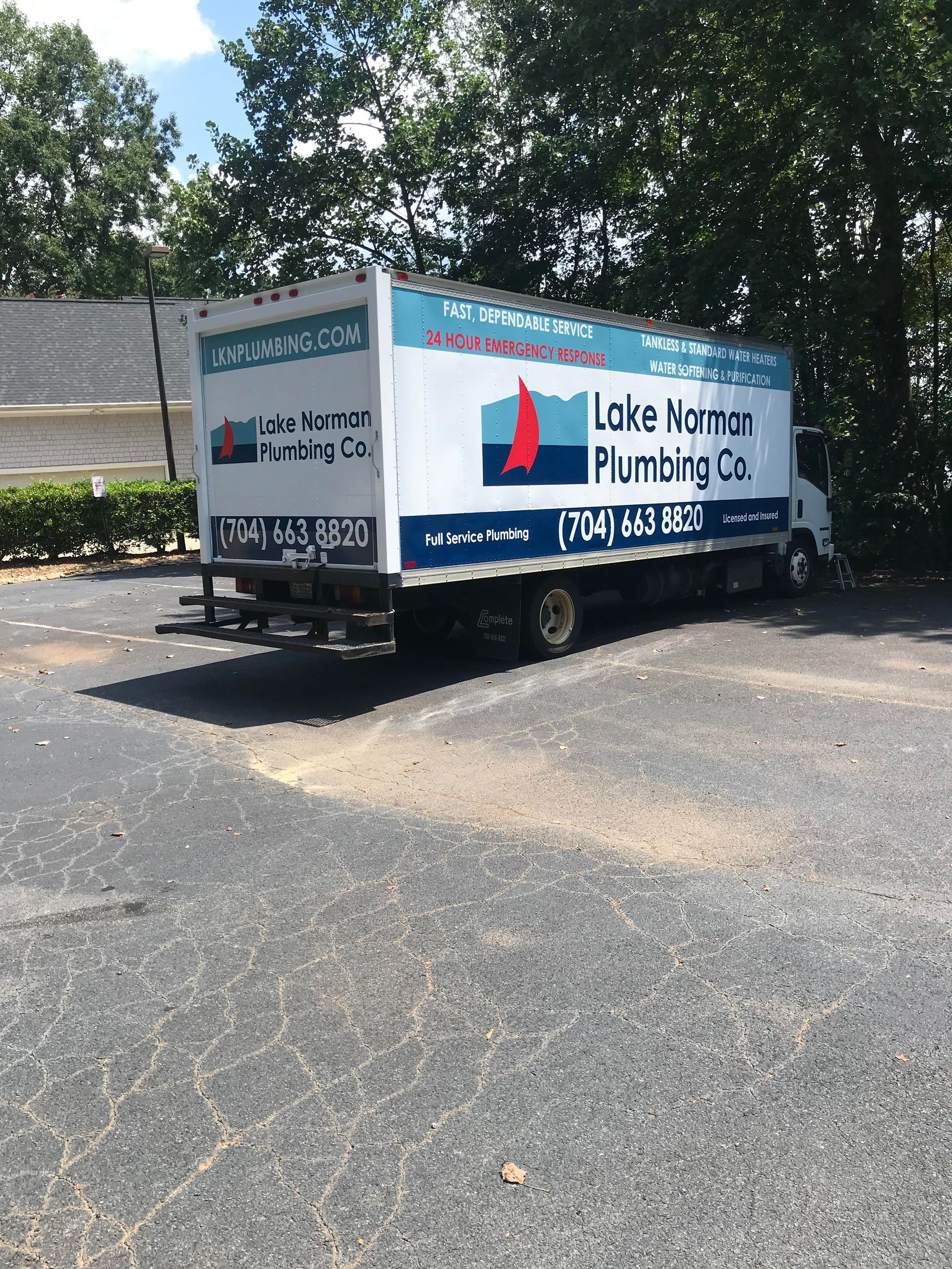 White utility trailer with Lake Norman Plumbing logo parked on asphalt under trees