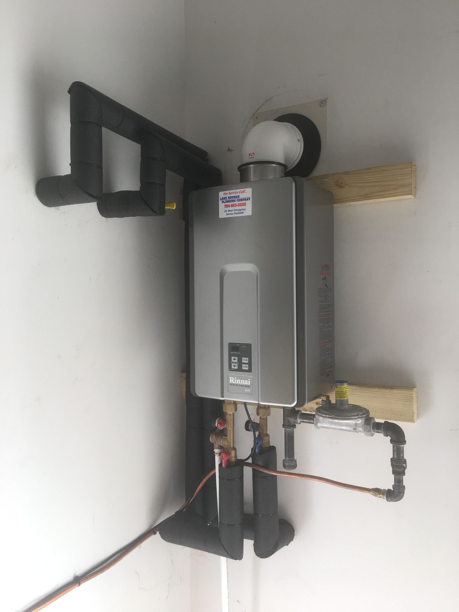 Wall-mounted gray water heater with black vent pipes in a utility nook