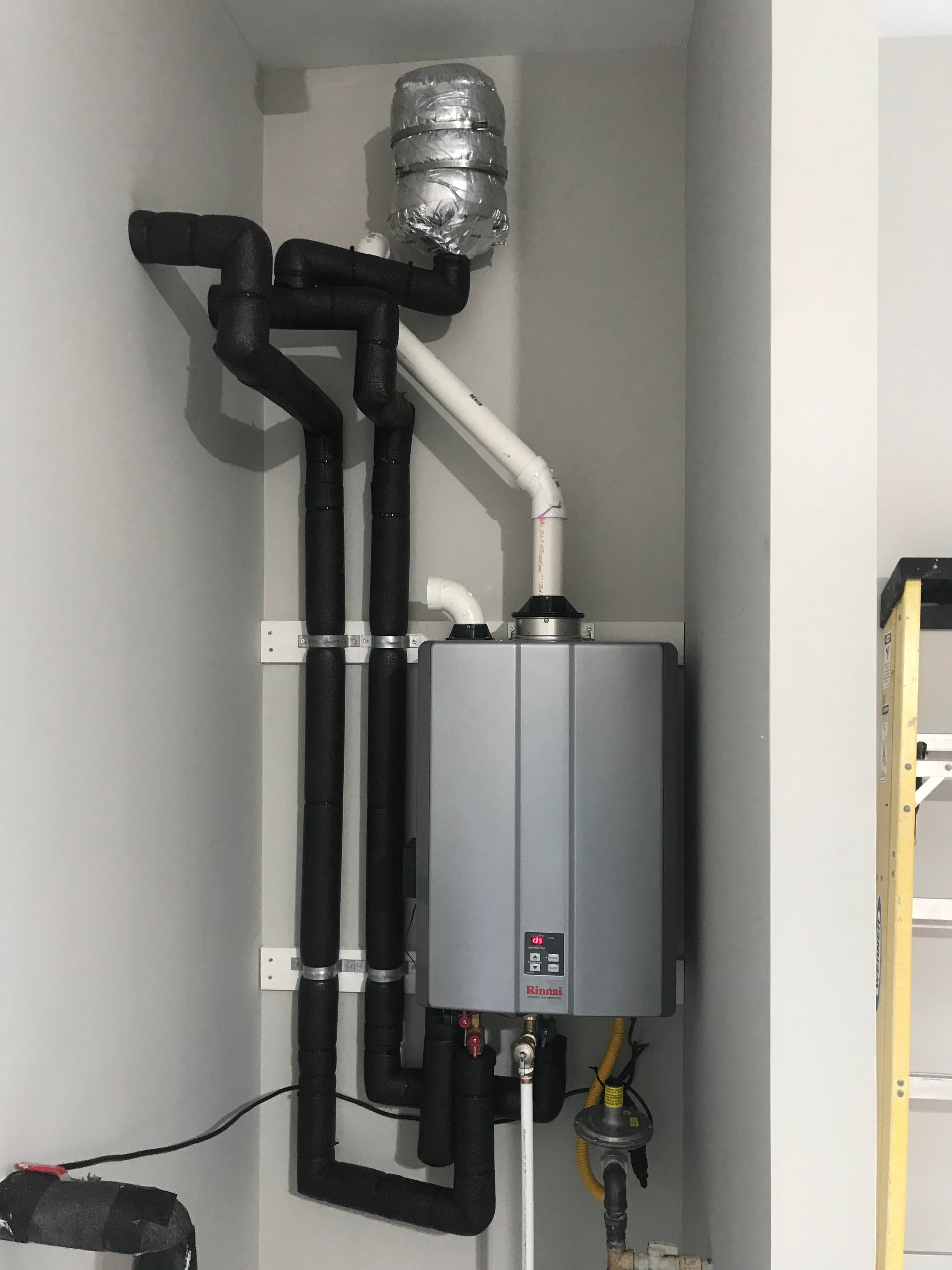 Wall-mounted water heater with black and white pipes in a utility closet