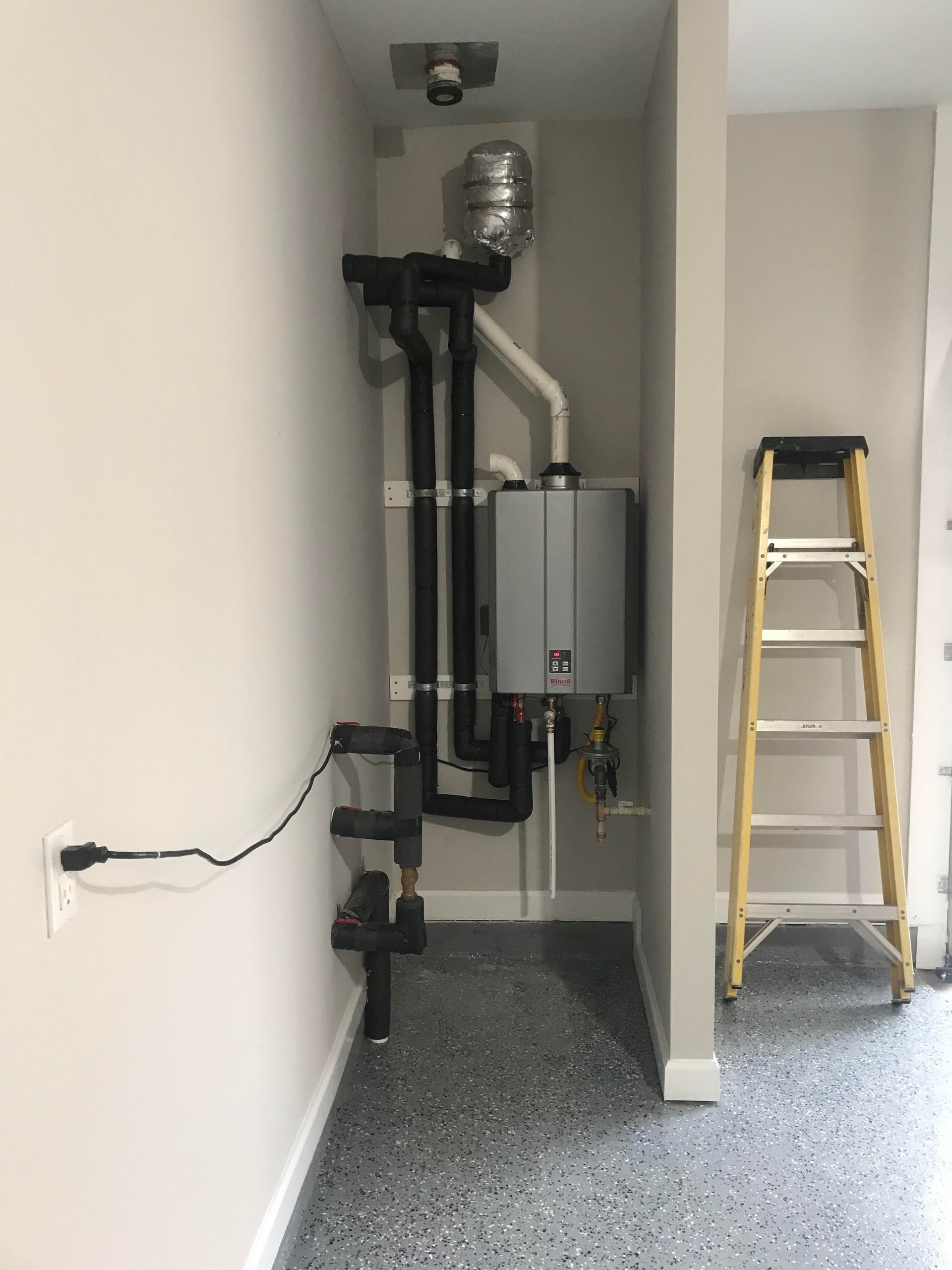 Utility room with plumbing equipment and a step ladder on a gray floor