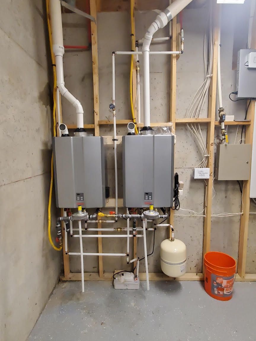 Two gray utility cabinets with exposed pipes, valves, and a white tank in a concrete utility room.