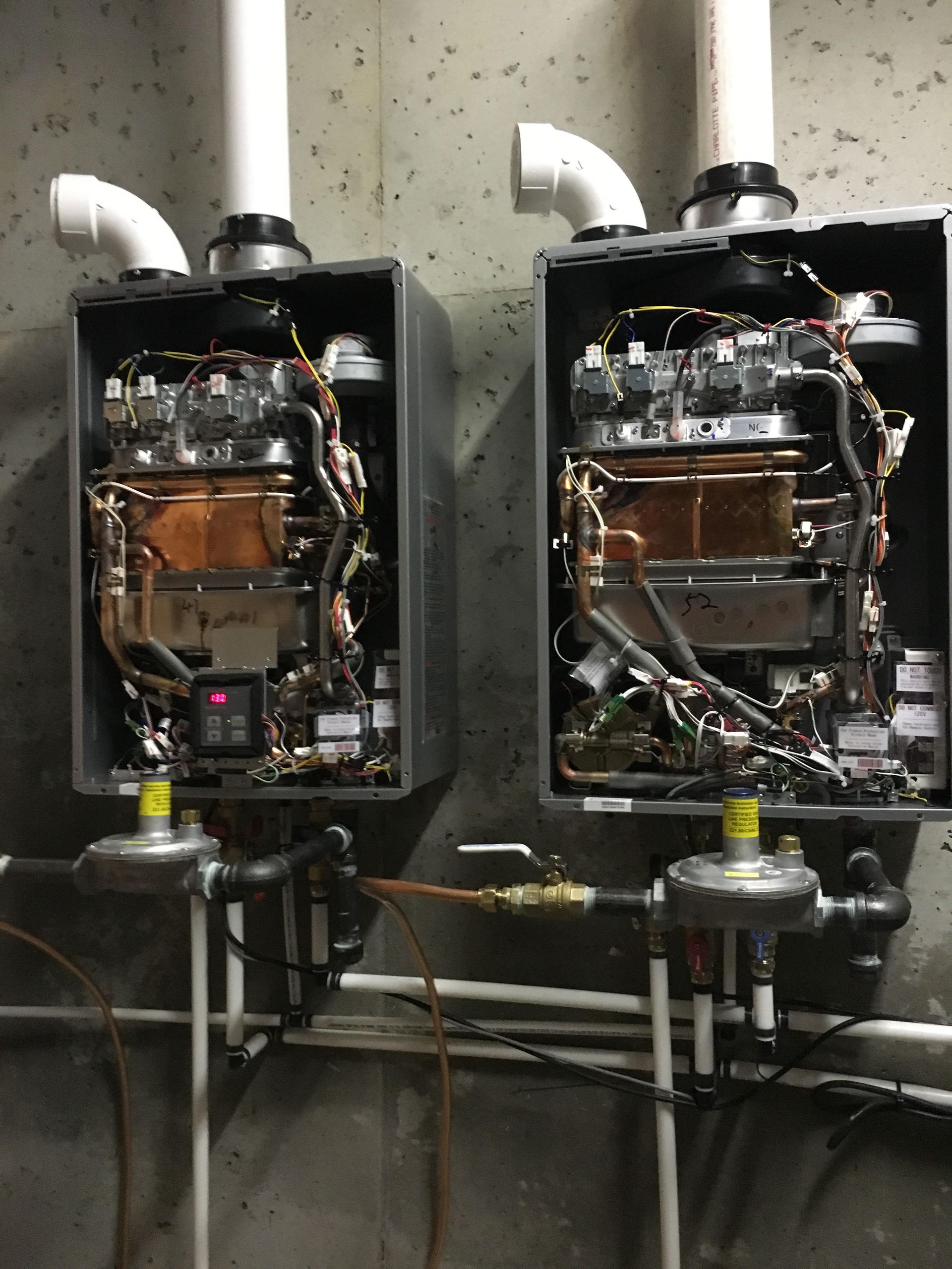Two industrial water heaters with exposed piping and vent pipes in a utility room.
