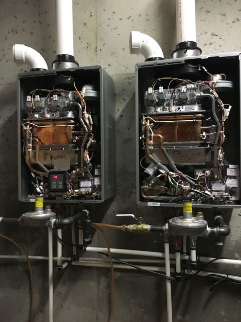 Two industrial water heaters with exposed piping and vent pipes in a utility room.