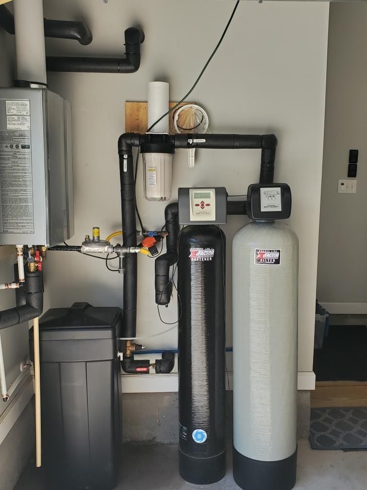 Water softener and filtration system with tanks and pipes in a utility room.