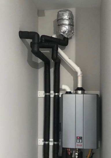 Wall-mounted boiler with black and white vent pipes in a utility closet