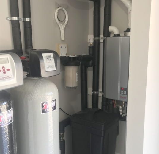 Indoor utility room with water treatment equipment, tanks, and a wall-mounted control unit.