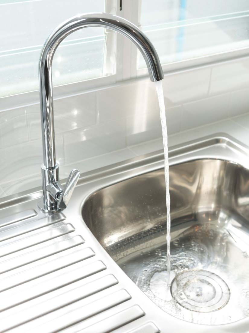 Chrome kitchen faucet running into a stainless steel sink beside a drying rack
