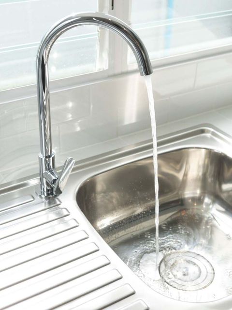 Chrome kitchen faucet running into a stainless steel sink beside a drying rack